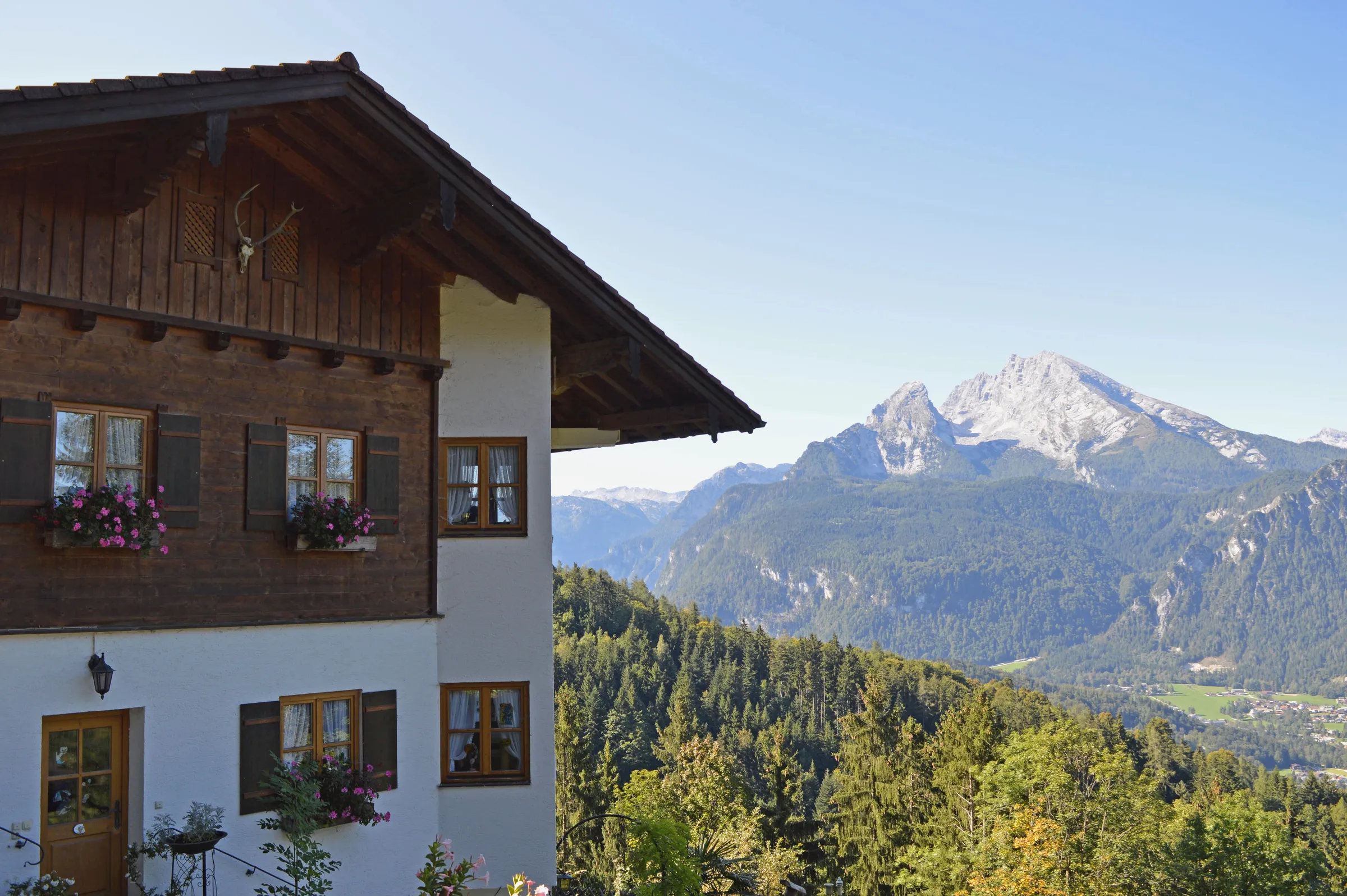 Ein Haus mit Holzgiebel und Blumenkästen vor Wald und Bergen im Sonnenlicht